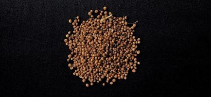 A spreaded dried coriander seed on black background. Ingredient background design. Available for text. Suitable for the food advertising of company and industry, poster, backdrop, flyer, etc. photo