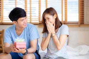 Beautiful young asian couple in love surprise gift box in bedroom at home, family anniversary with enjoy and romantic together wife and husband with relationship, Celebrating Valentine Day concept. photo