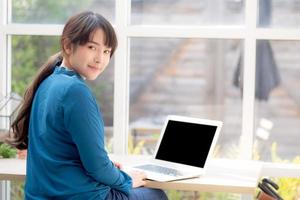 Beautiful of portrait asian young woman sitting looking camera and laptop on desk at coffee shop, professional female freelance working notebook computer connect internet online job, business concept. photo