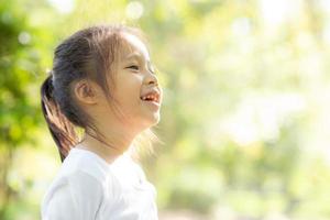 cara de retrato de linda niña asiática y felicidad y diversión infantil en el parque en verano, sonrisa y felicidad de niño asiático y relajación en el jardín, concepto de infancia de estilo de vida. foto