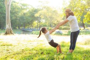 Young asian mother and little daughter playing the park with fun and happiness, family enjoy and relax and leisure together, mom and children smiling laughing in summer day. photo