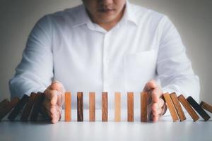 Risk management and business strategy concept, businessman hands stop the dominoes from falling continuously, preventing future risks from crisis. photo