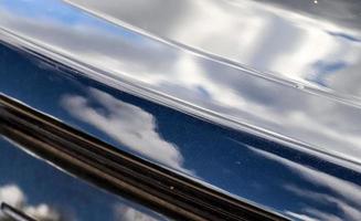 Reflections of a blue sky with clouds in the surface of a black sports car. photo