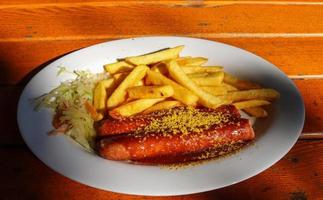 Traditional German currywurst, served with chips on a white plate. Wooden table as background. photo