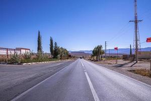 Straight asphalt road with markings against mountains in background photo