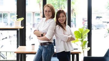 Two middle-aged women are looking at the camera while sitting on a desk in the office. female executives working in the office discussing documents photo