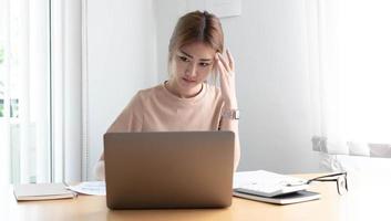 mujer asiática joven que siente tensión en la cabeza con migraña. mujer de negocios cansada y sobrecargada de trabajo mientras trabajaba en una computadora portátil en la oficina. foto