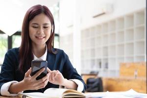 Asian woman talking on the phone and working on a laptop with a smiling face, Business Cell Phone Conversations, Working at cafe, cafe lifestyle, Stay cafe, New normal, learning, Social distancing. photo