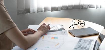 Close up of businesswoman or accountant using calculator to calculate calculate business data, working at office with paper document and laptop computer on office table, business and finance concept photo