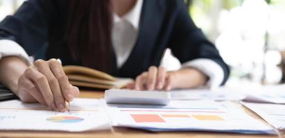 Close up of Hand business woman holding pen pointing on chart summary report and calculate finance. photo