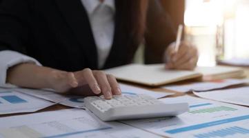 mano de mujer de negocios que sostiene la calculadora de uso de pluma y el punto del dedo en el gráfico de estadísticas de crecimiento y el gráfico en el papeleo para el análisis y cálculo de la contabilidad financiera del presupuesto. foto