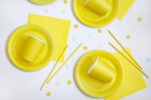 Yellow paper disposable plates, napkins and straws for drinks on white background. Table setting for picnic. Bright eco-court. Birthday, party and holiday concept. Top view, flat lay. photo