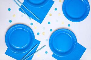 Blue paper disposable plates, napkins and straws for drinks on white background. Table setting for picnic. Bright eco-court. Birthday, party and holiday concept. Top view, flat lay photo