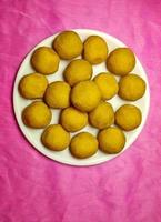 festival indio dulce - besan laddu, hecho con harina de gramo, azúcar y ghee, colocado en un plato blanco sobre un fondo de color. foto