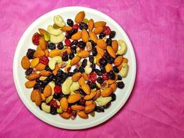 Las nueces y bayas sanas y nutritivas se colocan en un plato blanco sobre un fondo de color. foto