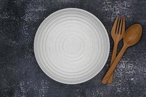 un plato vacío redondo blanco con tenedor y cuchara sobre fondo oscuro para el concepto de alimentos e ingredientes configurado foto