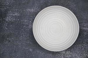 A white round empty plate on grunge dark background for food and ingredient concept set up photo