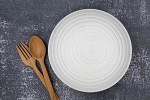 un plato vacío redondo blanco con tenedor y cuchara sobre fondo oscuro para el concepto de alimentos e ingredientes configurado foto