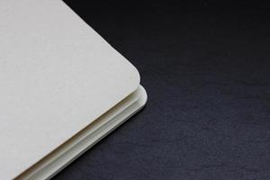 White closed notebook corner lying on dark background, horizontal photo. Stationery, empty pages for notes, blank paper sheets, office and business concept photo