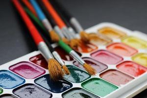 Various brushes lying on white watercolor palette, closeup, blurred background, horizontal photo. Artist's tools for drawing, bright different colors, selective focus photo