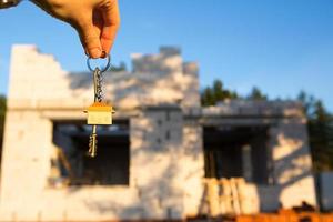 Hand with the key to the future house on the background of a construction site and walls made of porous concrete block. Building a home, moving to a new cottage, farm in the countryside photo