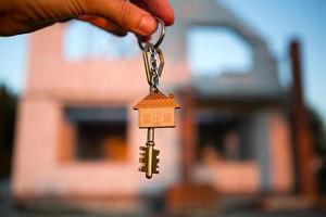 Hand with the key to the future house on the background of a construction site and walls made of porous concrete block. Building a home, moving to a new cottage, farm in the countryside photo