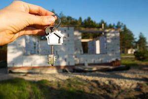 Hand with the key to the future house on the background of a construction site and walls made of porous concrete block. Building a home, moving to a new cottage, farm in the countryside photo