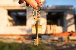 Hand with the key to the future house on the background of a construction site and walls made of porous concrete block. Building a home, moving to a new cottage, farm in the countryside photo
