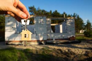 Hand with the key to the future house on the background of a construction site and walls made of porous concrete block. Building a home, moving to a new cottage, farm in the countryside photo