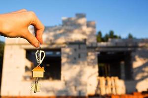 Hand with the key to the future house on the background of a construction site and walls made of porous concrete block. Building a home, moving to a new cottage, farm in the countryside photo