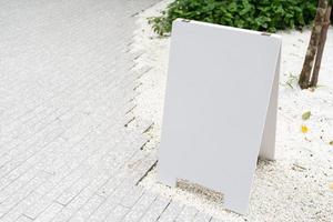 white mock up wooden sign board on concrete floor. Blank white sign outside in daytime. photo