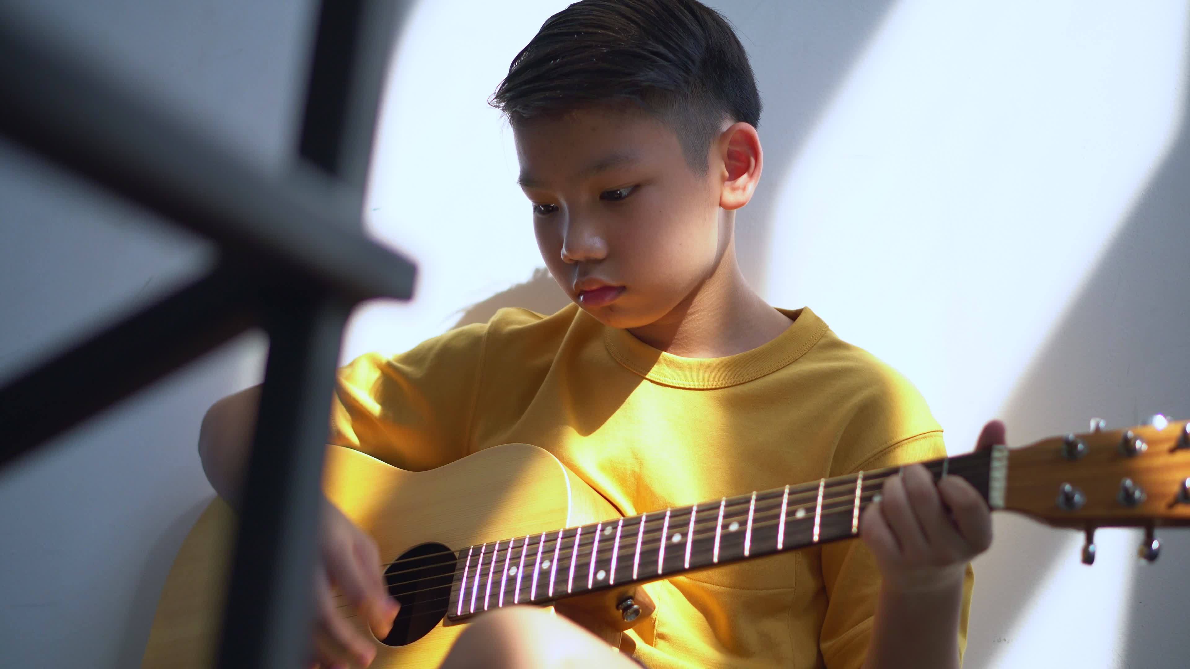Preteen Asian boy playing acoustic guitar dressed sitting on the cozy sofa at the home living room and enjoying a favorite hobby, Music education concept image. 8157548 Stock Video at Vecteezy