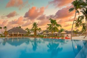 Luxury sunset over infinity pool in a summer beachfront hotel resort at tropical landscape. Tranquil beach holiday vacation background mood. Amazing island sunset beach view, palms swimming pool photo