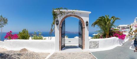 Fantastic summer vacation landscape. Santorini white architecture with iron gate and pink flowers. Tranquil travel background, luxury tourism scenery, stone stairs under blue sky. photo