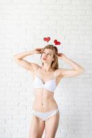 Slim sexy young woman in white underwear wearing heart shaped headband on white brick wall background photo