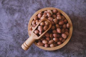 Raw Groundnuts in the wooden bowl on cement background. Top view. photo