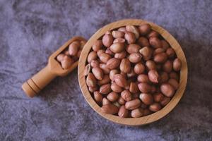 Raw Groundnuts in the wooden bowl on cement background. Top view. photo