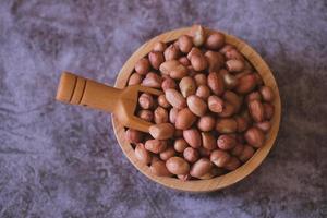 Raw Groundnuts in the wooden bowl on cement background. Top view. photo