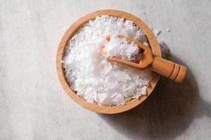 Flower of salt, is a salt that forms as a thin, delicate crust on the surface of seawater in the wooden scoop and wooden bowl on wooden background. Selective focus. photo