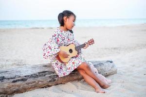 joven asiática tocando el ukelele en la playa. foto