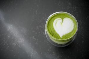 Top view of hot matcha green tea latte art in double walled glass on table in the cafe. Flat lay. photo