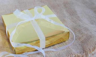 caja de regalo dorada con cinta blanca en el saco marrón foto