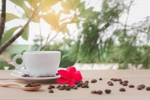 A white coffee cup with a saucer and spoon is placed on a wooden plate on the landscape nature background. photo