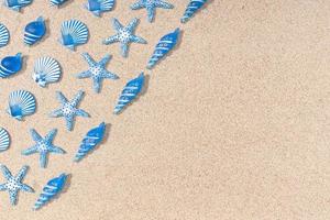 Summer background with blue seashell pattern on beach sand background. Copy space. Top view photo