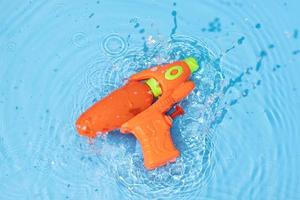 Water gun toy splashing on blue water surface. Fun, leisure summertime background photo