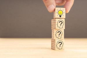Creative idea and innovation concept. hand picking a wooden block with light bulb icon and human head with question mark inside. Copy space photo