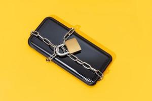 Phone security concept. Smartphone locked with chain and padlock on yellow background. Mobile security and data privacy photo