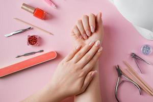 procedimiento de cuidado de uñas en un salón de belleza. manos femeninas y herramientas para manicura sobre fondo rosa. concepto de cuidado corporal spa. foto