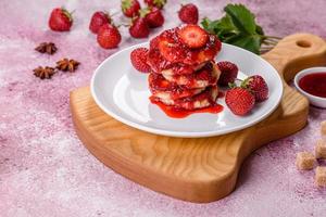 tortitas de requesón con fresas en rodajas y mermelada de fresa en un plato sobre un fondo de hormigón foto