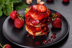 Cottage cheese pancakes with sliced strawberries and strawberry jam on a plate on a concrete background